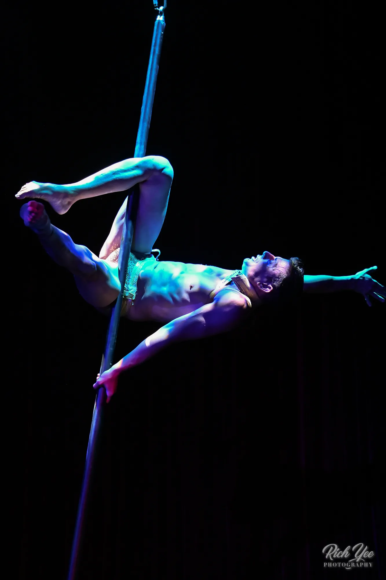 Male Chinese pole acrobat under blue spotlight