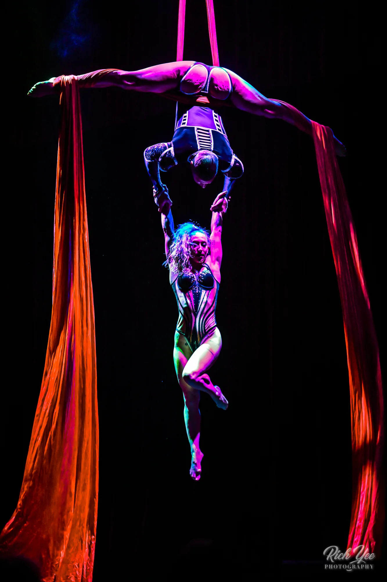 Duo aerial silks split pose in orange light